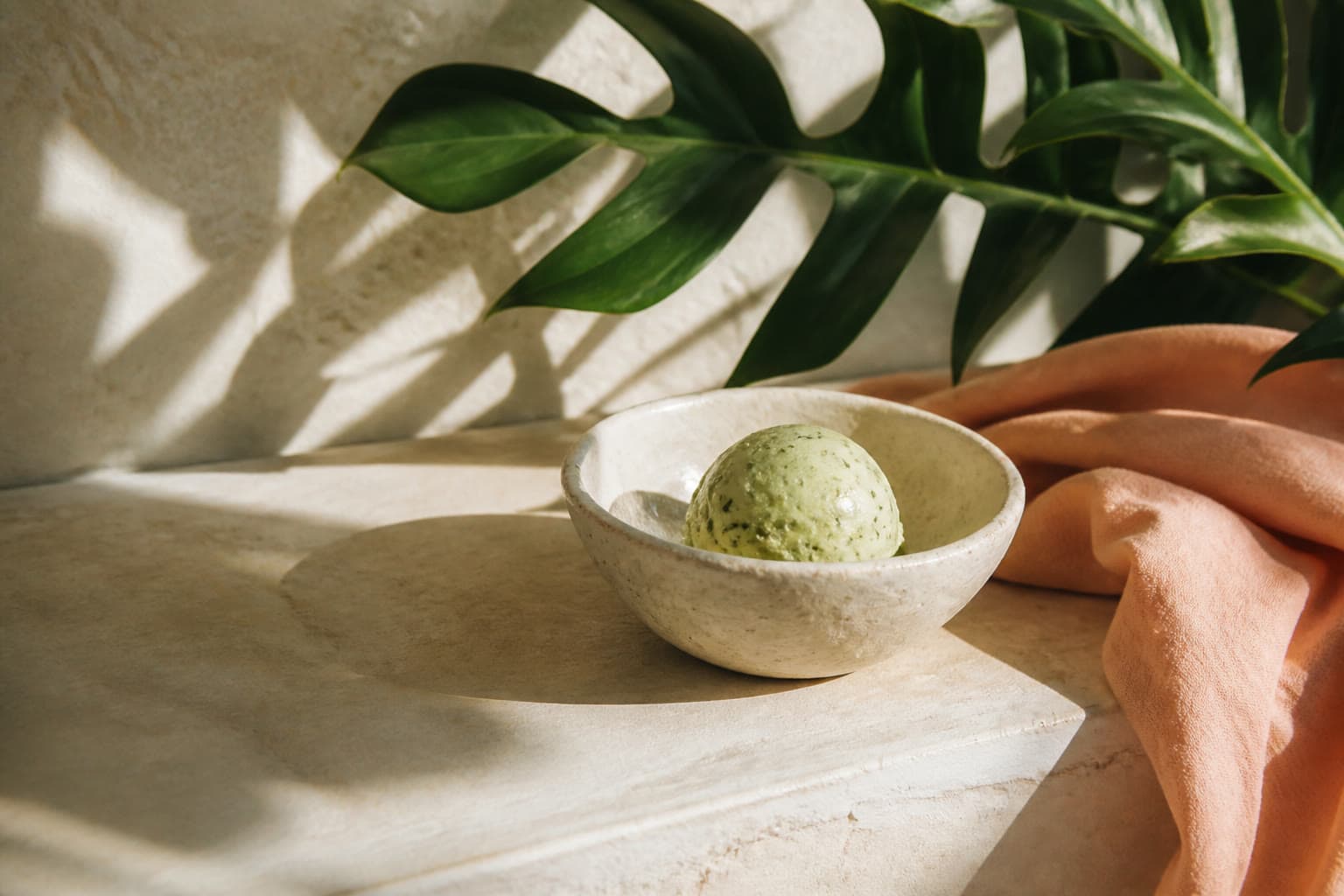 A pale green scoop in a handmade bowl, beside a broad leaf